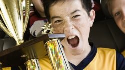 A group of boys in soccer team shirts holding a trophy and celebrating a win. In a team bus.