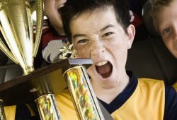A group of boys in soccer team shirts holding a trophy and celebrating a win. In a team bus.
